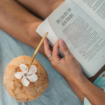 Lesende Frau mit geöffnetem Buch und einer Trink-Kokosnuss | "Da gibt's noch mehr – Deine Kokosstimme" aus dem marly books Verlag mit der Autorin Theresa Sophie